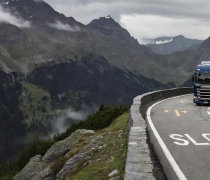 Camion sur une route montagneuse européenne, falaises et lac en contrebas